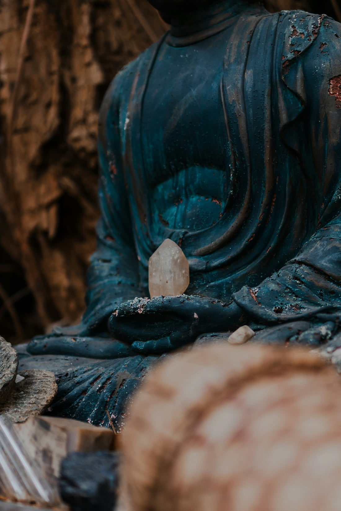 Buddha statue holds crystal; weathered, peaceful, spiritual